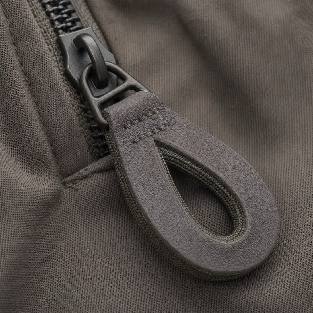 Close-up of an oversized loop zip pull: a flat oval loop wide enough to hook a finger through, fitted to a matte zip slider.
