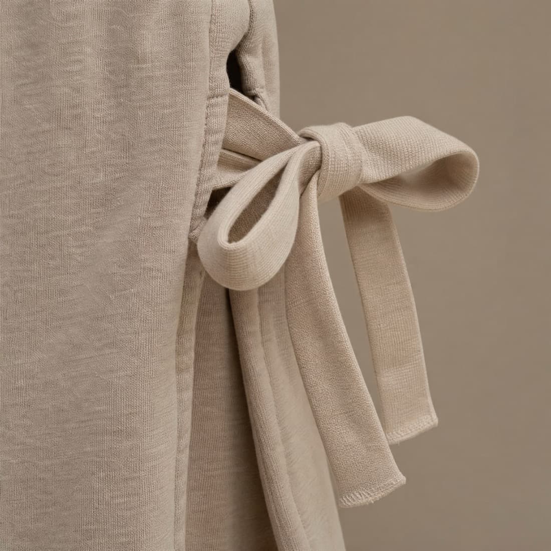 Close-up of a flat cotton tape closure at a side seam, two wide soft tapes loosely knotted.