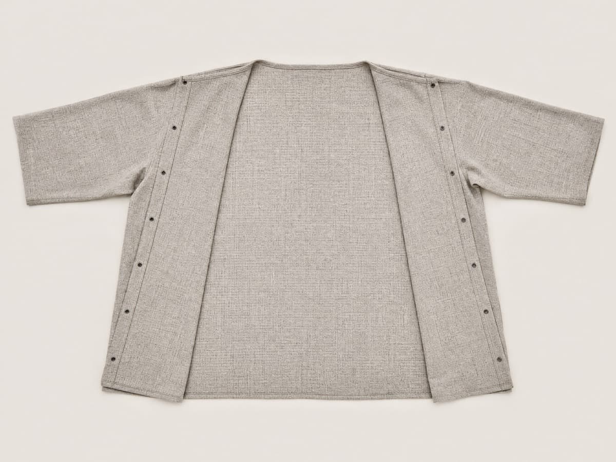 A warm grey woven top laid flat with both side seams closed, reading as an ordinary relaxed top with no visible fasteners at the front.