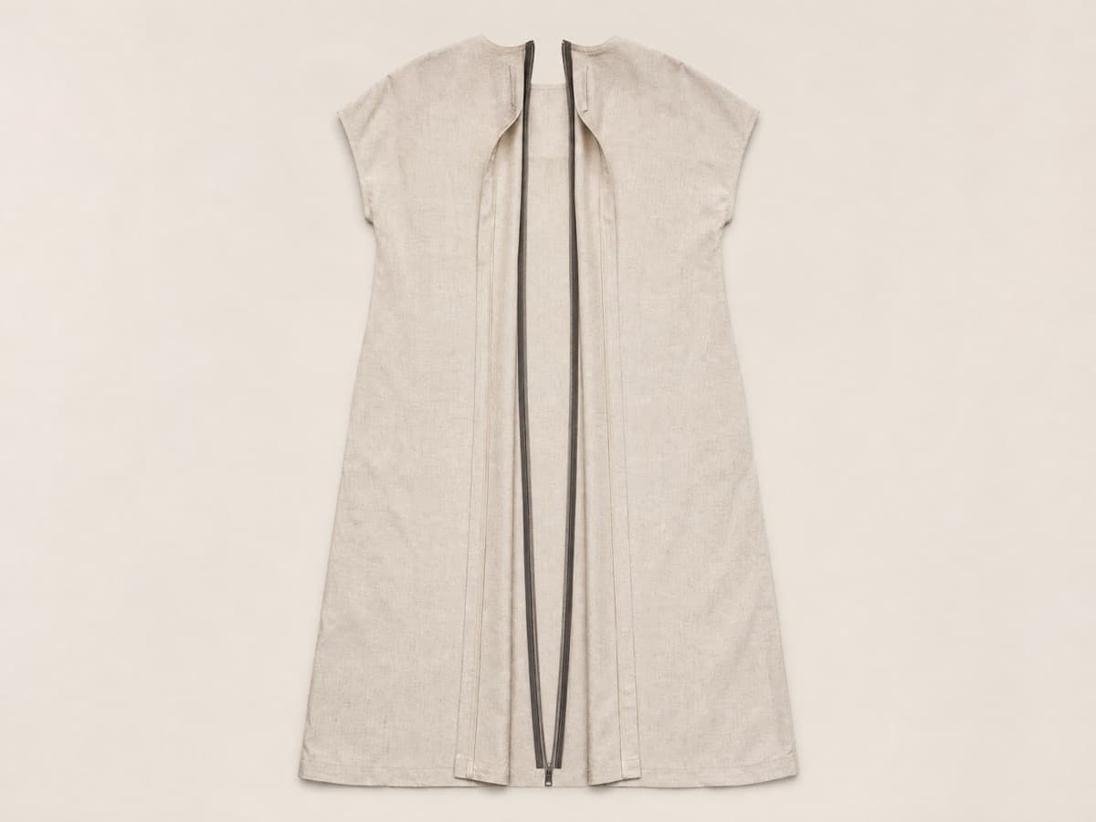 A mid-length oatmeal dress laid flat and seen from the back, with a full-length centre-back opening from neckline to hem, the panels opened slightly.