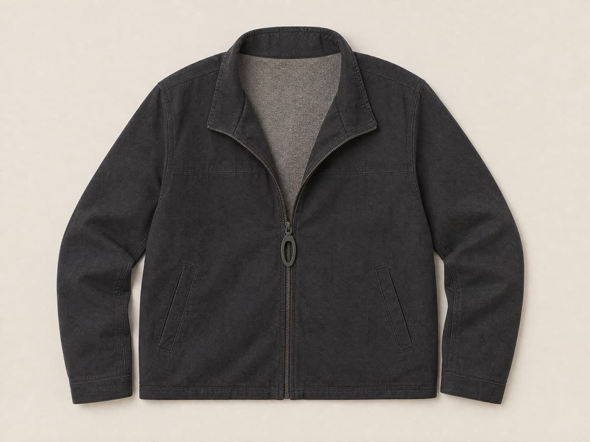 A charcoal jacket laid flat with a matte front zip fitted with an oversized flat oval loop pull, the zip half opened.